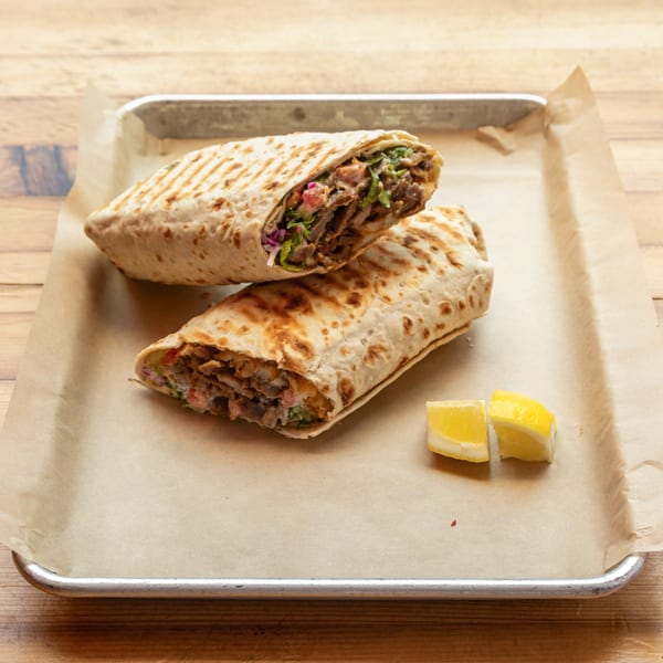 Two grilled doner wraps with meat, vegetables, and sauce, served with lemon wedges.