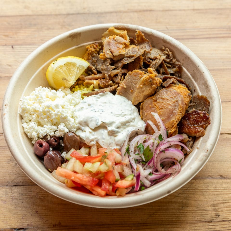 A Turkish doner bowl with meat, rice, feta, olives, red onion, tomato, and tzatziki sauce.