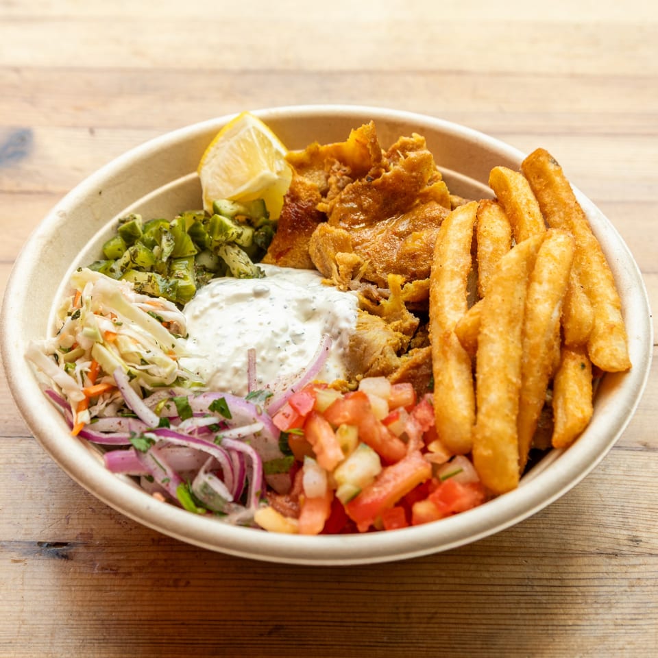 A Turkish doner bowl with fried chicken, fries, coleslaw, salsa, and a lemon wedge.