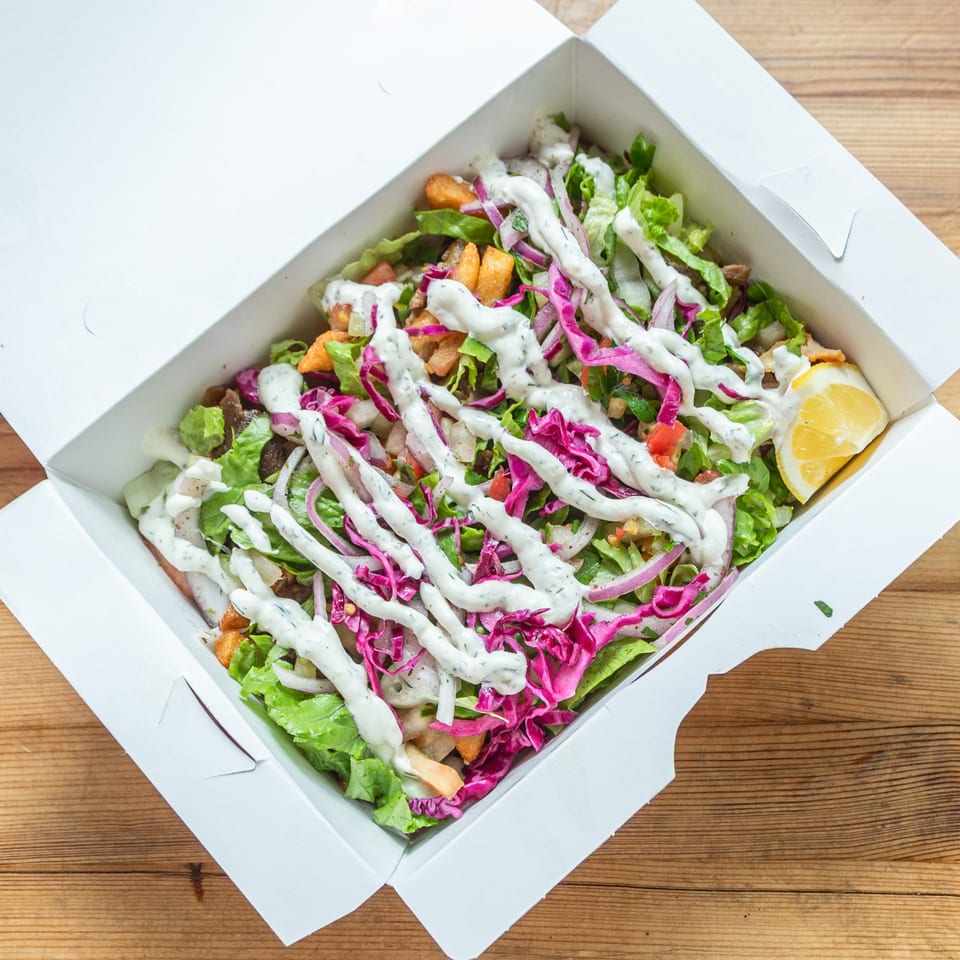 A Turkish doner salad with lettuce, red cabbage, onions, and white sauce in a takeout box.