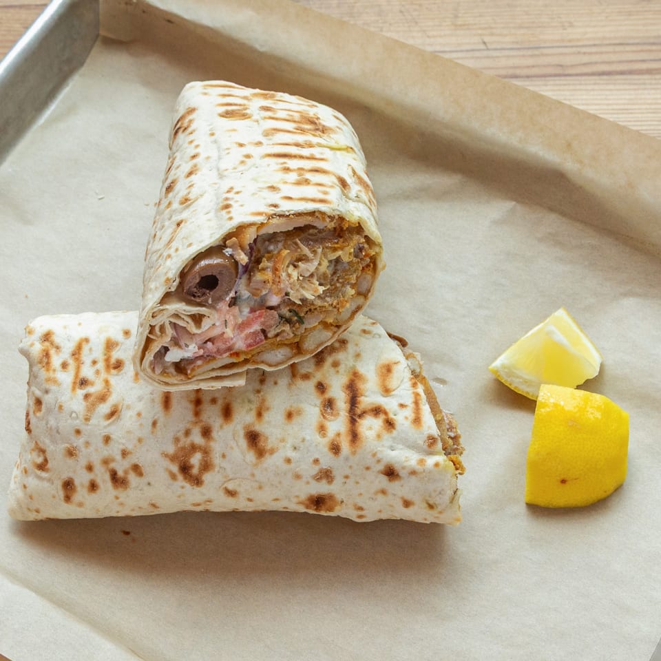 Two Naughty Doner wraps, one sliced open, with lemon wedges on a tray.