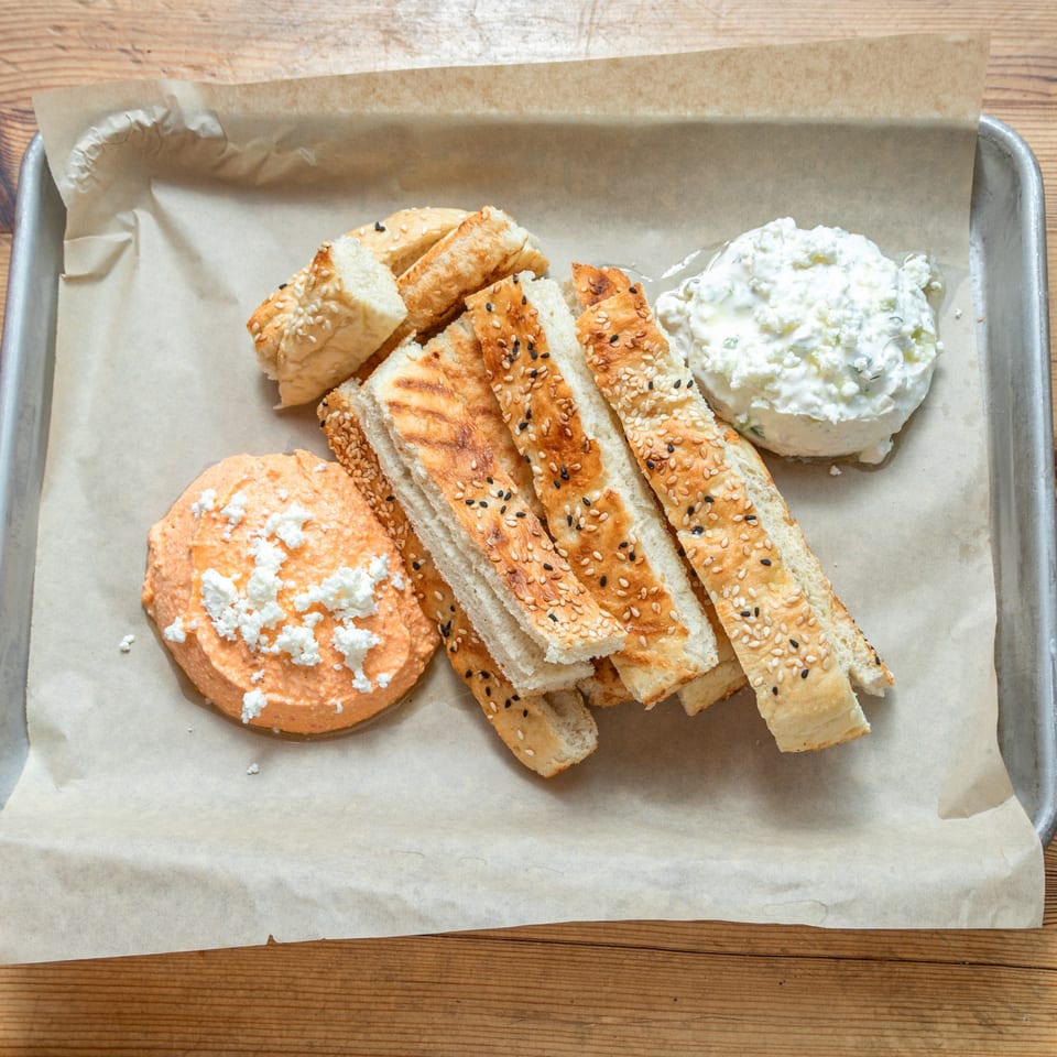 Turkish bread sticks with sesame seeds, served with two dips on a metal tray.