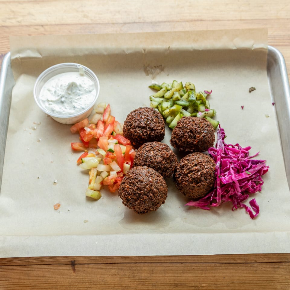 Turkish falafel with chopped tomatoes, cucumbers, red cabbage, and a side of white sauce.